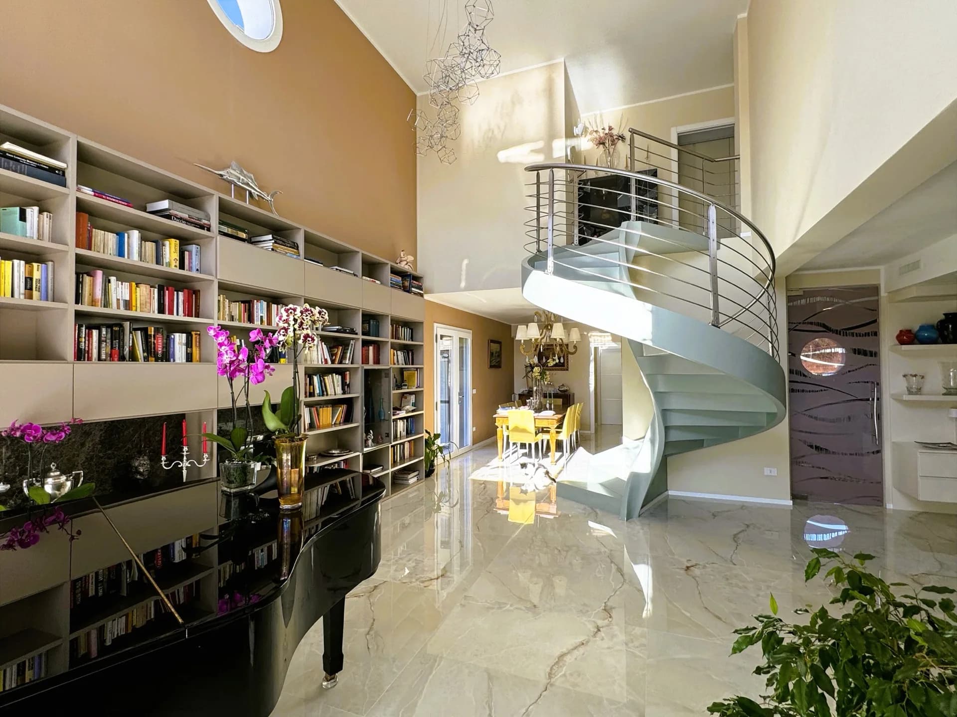 Completed villa interior with central staircase, full library wall and marble flooring